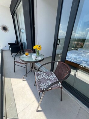 Een balkon met een glazen tafel en stoelen, een vaas met gele bloemen en uitzicht op zee.