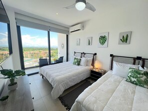 Een hotelkamer met twee bedden, een balkon en een uitzicht, plus een plafondventilator.