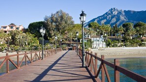 A wooden boardwalk leading to a beach with palm trees and a mountain in the background. - SR Reserva de Marbella 1803 2-Bedroom Penthouse (Marbella)