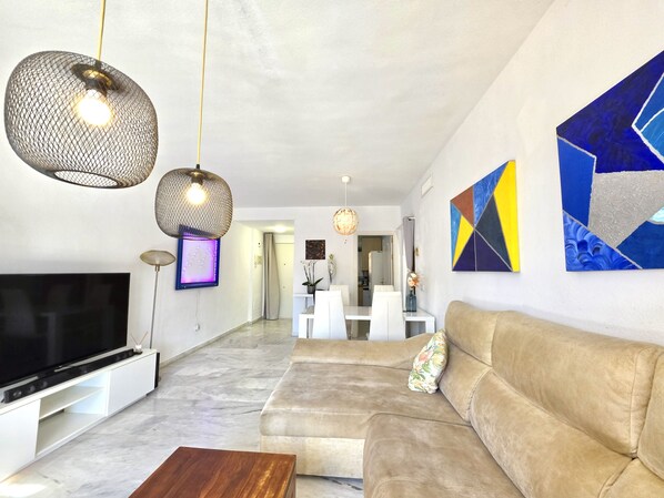 A modern living room with a flat-screen TV, a beige sofa, and a coffee table. - SR Reserva de Marbella 1803 2-Bedroom Penthouse (Marbella)