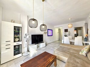 A modern living room with a flat-screen TV, a white cabinet with glass doors, a standing fan, and a wooden coffee table. - SR Reserva de Marbella 1803 2-Bedroom Penthouse (Marbella)