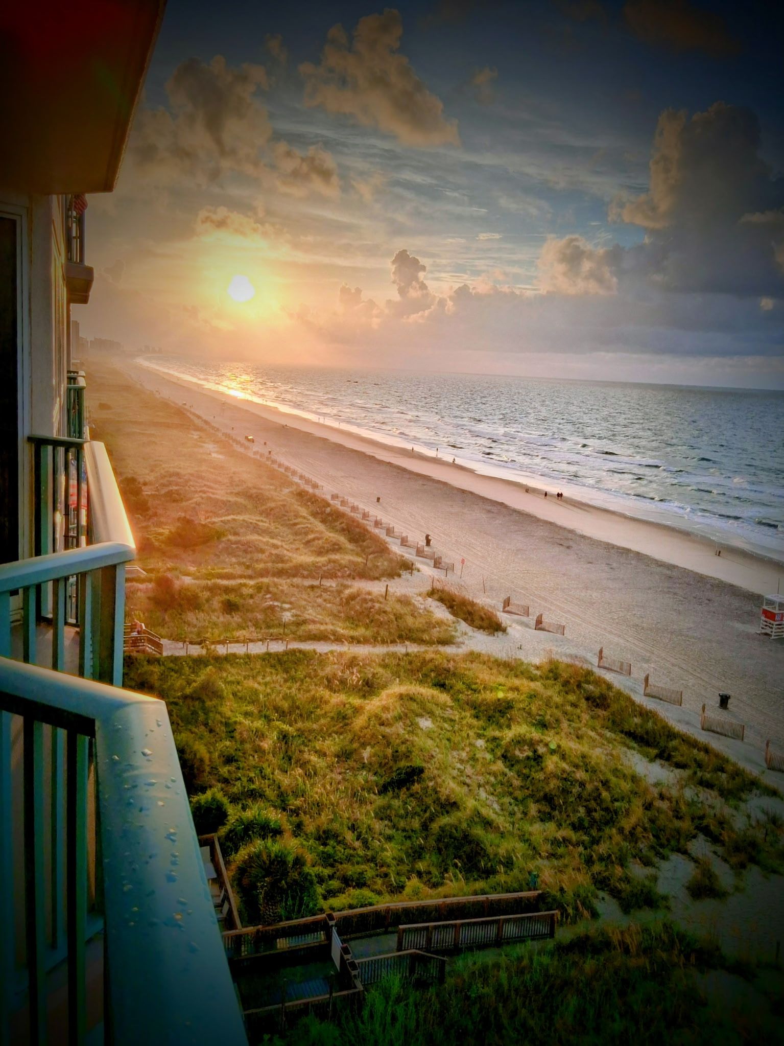 Une vue sur la plage depuis un balcon, avec un ciel dégagé et le soleil se couchant ou se levant.