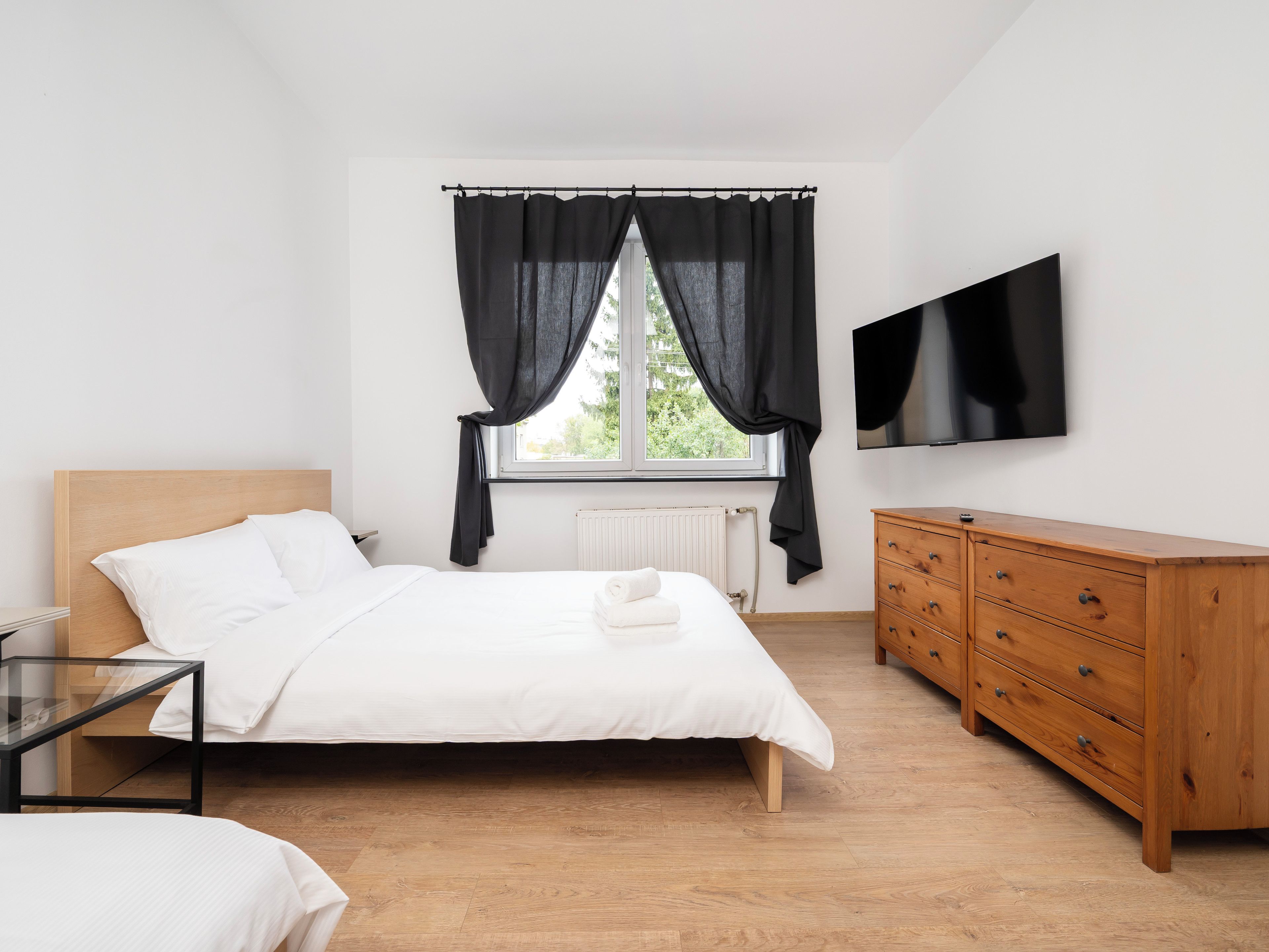 A bedroom with a bed, a dresser, a TV, and a window with curtains.
