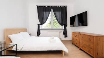 A bedroom with a bed, a dresser, a TV, and a window with curtains.