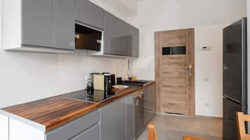 A modern kitchen with grey cabinets, a wooden countertop, and a stainless steel refrigerator.
