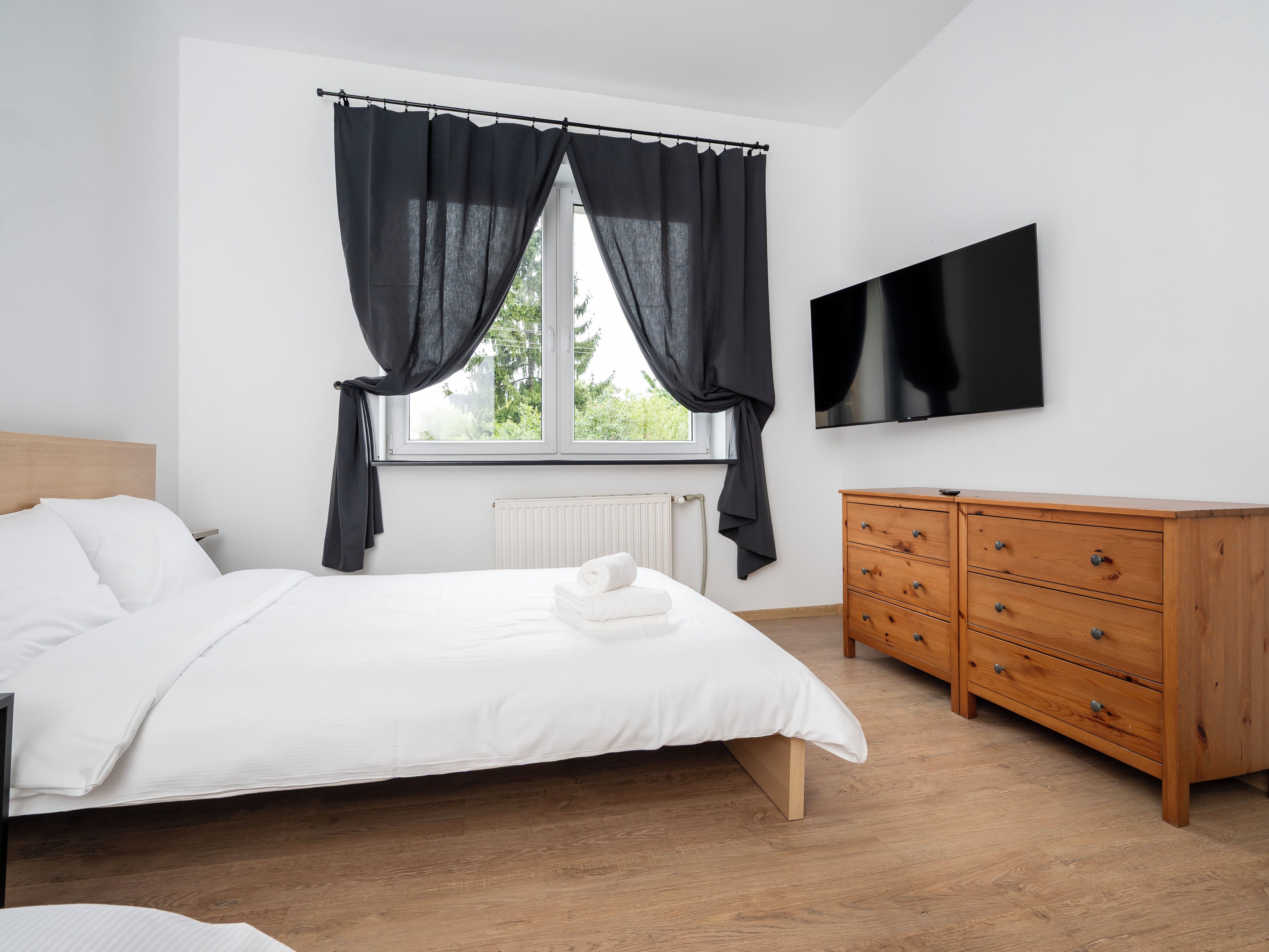Un dormitorio con cama, cómoda, televisor y ventana con cortinas.