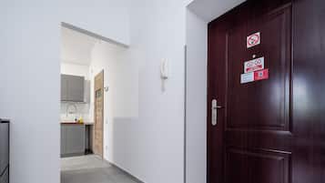 A hallway with a wooden door, a kitchen area, and a white wall with a phone and signs.