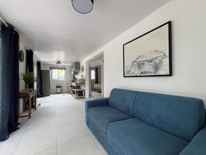 Ein modernes Wohnzimmer mit einem blauen Sofa, einem großen abstrakten Gemälde und einer Küchenzeile im Hintergrund.
