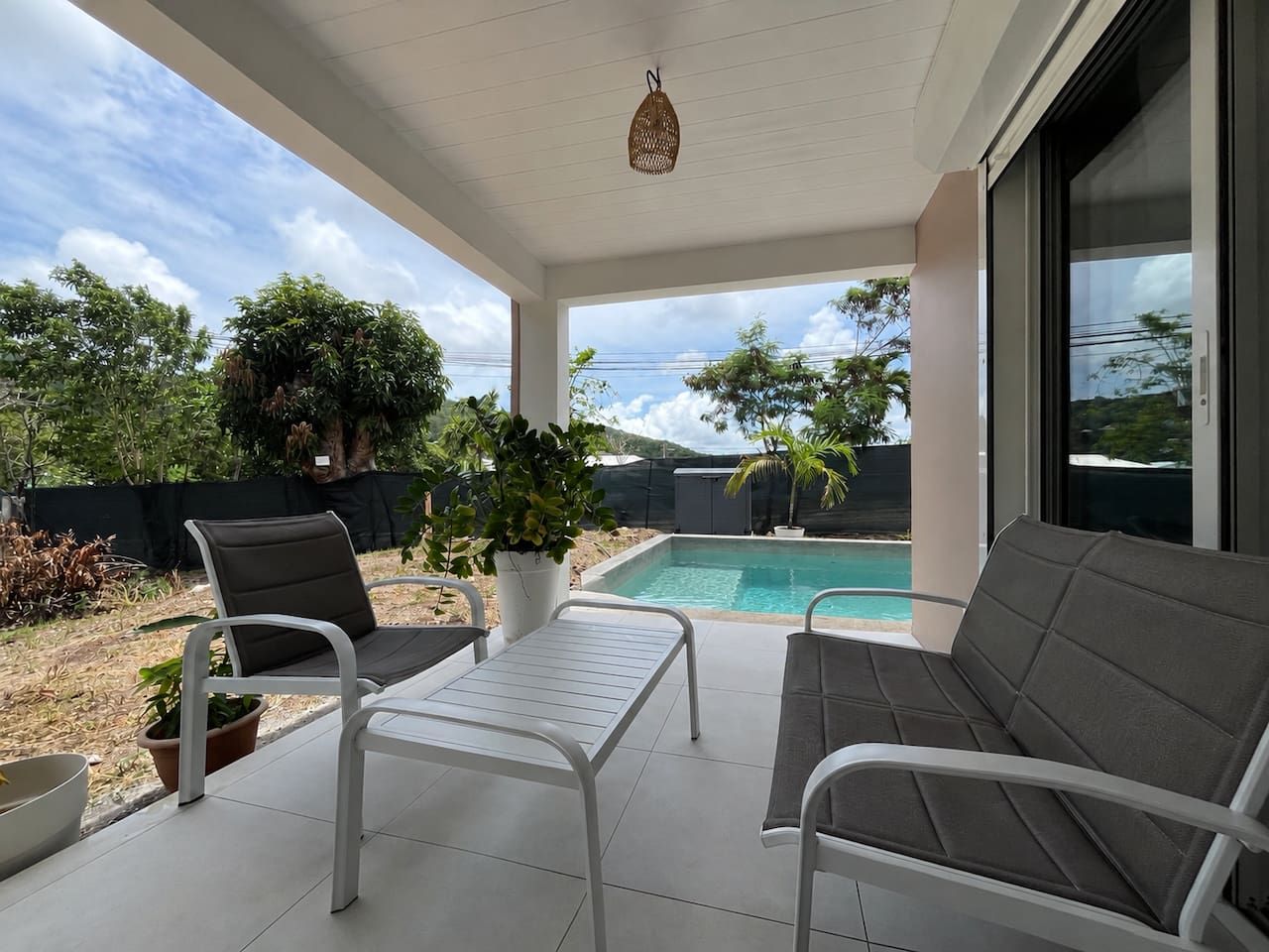 A covered outdoor area with a pool, seating, and potted plants.
