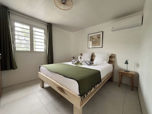 Ein Schlafzimmer mit einem hölzernen Bett, einer grünen Tagesdecke, einer Wandklimaanlage und einem kleinen Nachttisch mit Lampe.