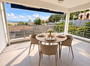 A dining area with a round table set for four, surrounded by chairs, on a balcony with a view of the cityscape. - Evana · Terrace with bay view · Parking · Air conditioning (Fort-de-France)