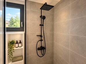A shower with a handheld showerhead and a wall-mounted panel, a window with a view of trees, and a shelf with toiletries. - Evana · Terrace with bay view · Parking · Air conditioning (Fort-de-France)