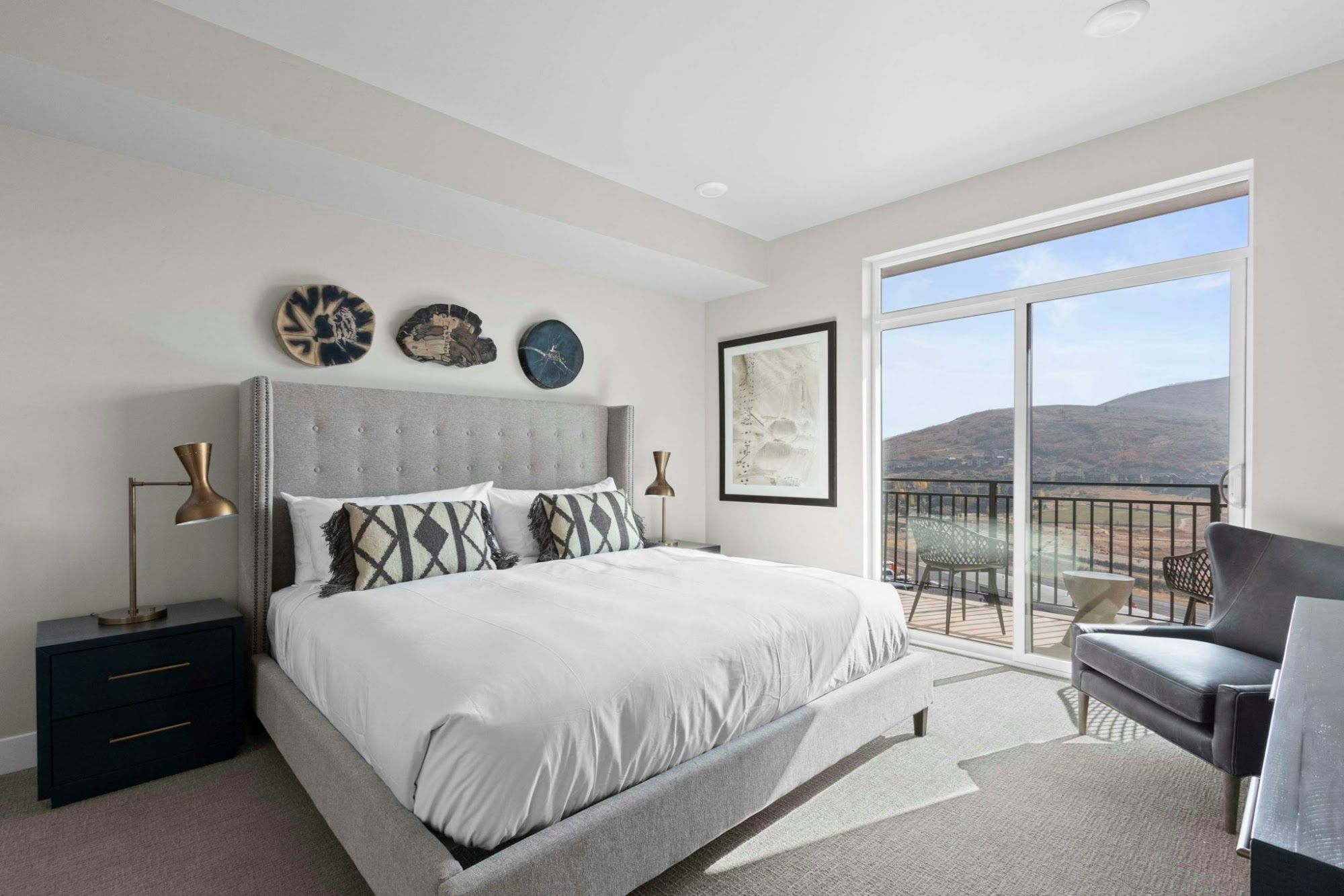 A bedroom with a large bed, a nightstand, a desk, and a balcony with a view.