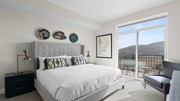 A bedroom with a large bed, a nightstand, a desk, and a balcony with a view.