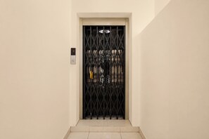 Un couloir avec une grille en métal noir et un panneau de commande numérique pour l’ascenseur.