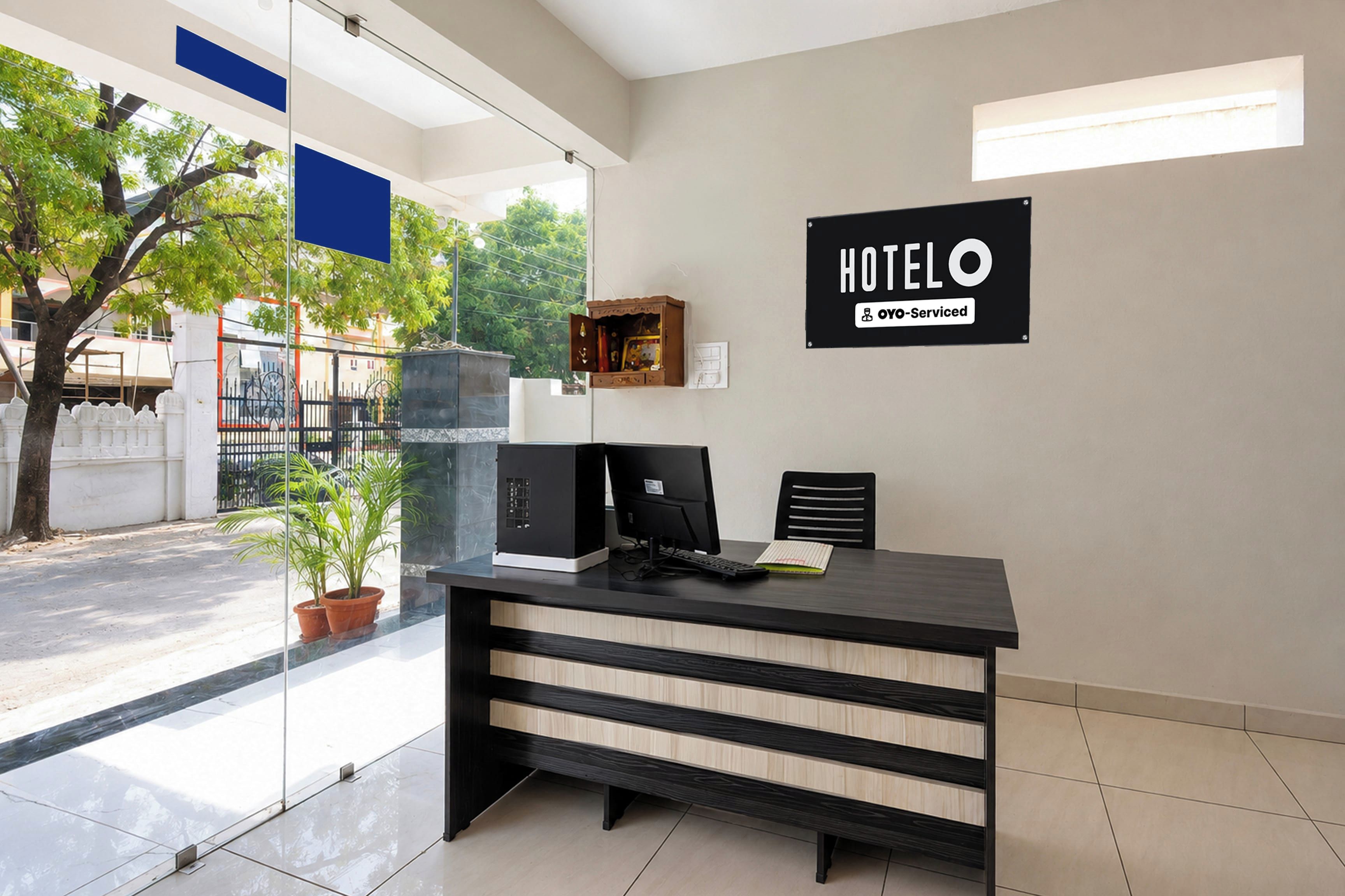 A hotel reception desk with a computer, a small cabinet, and a sign indicating it is an OYO-Serviced hotel.