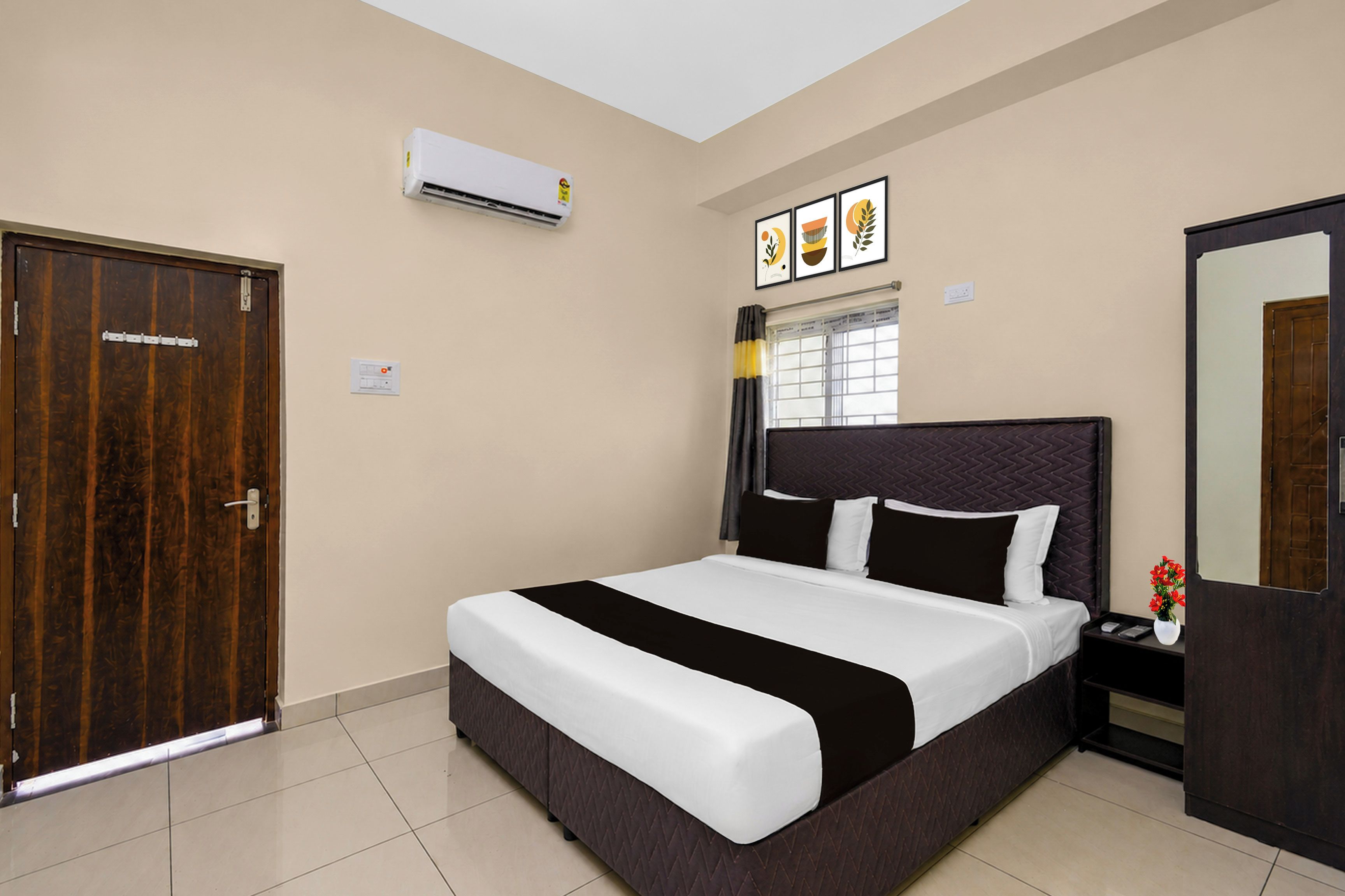 A hotel room with a bed, a wardrobe, an air conditioning unit, a window with curtains, and a wall-mounted artwork.