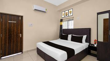 A hotel room with a bed, a wardrobe, an air conditioning unit, a window with curtains, and a wall-mounted artwork.