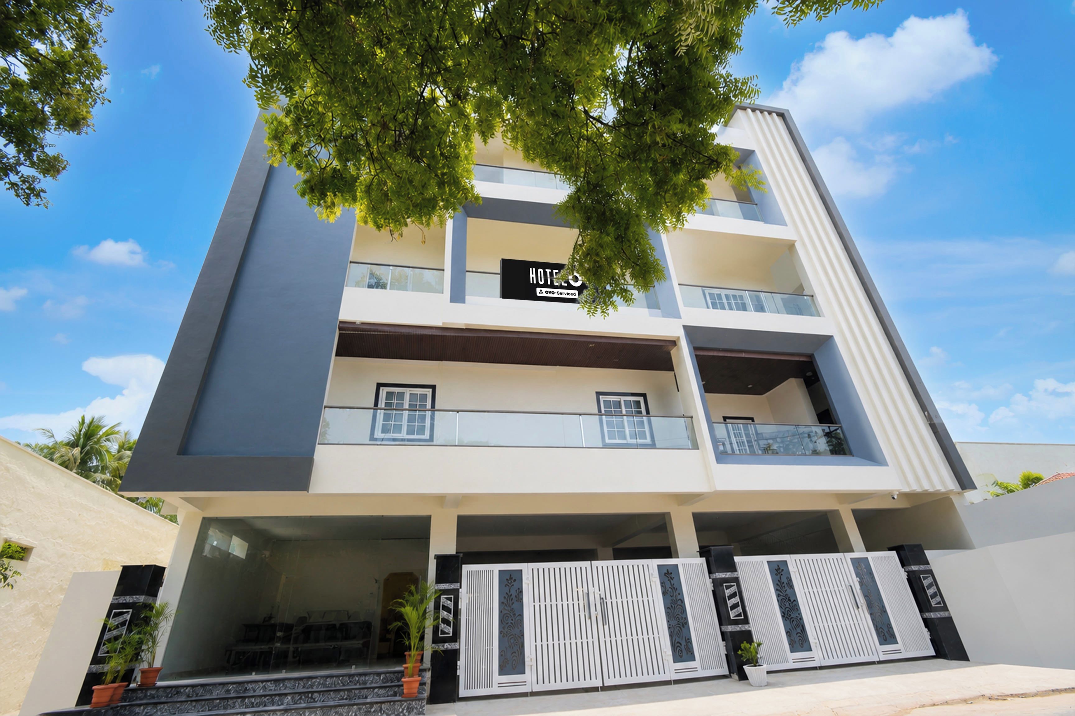 A multi-story hotel with a modern design, featuring balconies on each floor and a gated entrance.