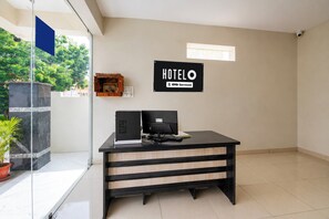 A reception desk with a sign indicating it's serviced by OYO, a hotel with a modern design, a glass partition, and a view of greenery outside.
