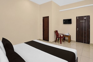A hotel room with a bed, a desk with a chair, a television, and two doors.