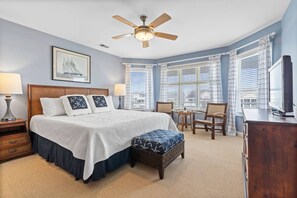A hotel room with a large bed, a ceiling fan, a television, and a view of the city through the windows. - Waterfront 5br/4.5ba Canal Home Close to The Beach (Ocean Isle Beach)