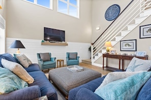 A spacious living room with a large couch, two armchairs, a coffee table, and a staircase with a decorative wall piece. - Waterfront 5br/4.5ba Canal Home Close to The Beach (Ocean Isle Beach)