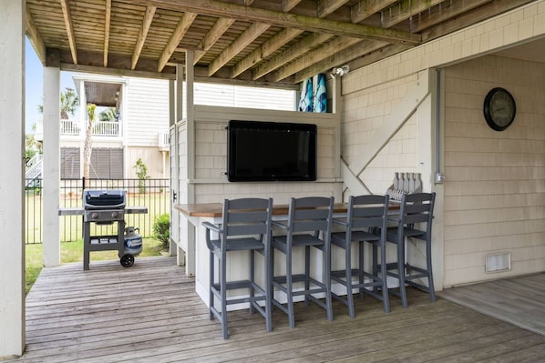 An outdoor patio with a built-in grill, a flat-screen TV, and a seating area with chairs. - Waterfront 5br/4.5ba Canal Home Close to The Beach (Ocean Isle Beach)
