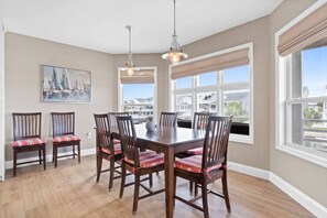 A dining area with a wooden table and chairs, large windows with blinds, and a painting on the wall. - Waterfront 5br/4.5ba Canal Home Close to The Beach (Ocean Isle Beach)