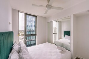 Een hotelkamer met een bed, een groen bekleden hoofdeinde, een plafondventilator, een groot raam en een spiegel die het bed reflecteert.