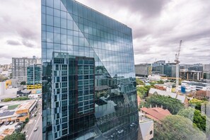 Een modern glazen gebouw met een reflecterend oppervlak, omringd door stedelijke infrastructuur en bouwkranen.