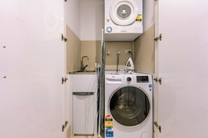 A compact laundry room with a front-loading washing machine, a small sink, and a wall-mounted dryer. - Bright 2 Bedroom Escape with Stunning City Views (Fortitude Valley)