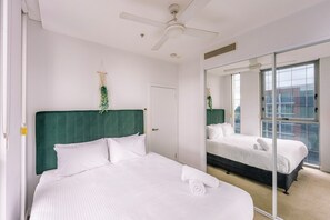 A hotel room with a large bed, a ceiling fan, a window with a view, and a mirror reflecting the room. - Bright 2 Bedroom Escape with Stunning City Views (Fortitude Valley)