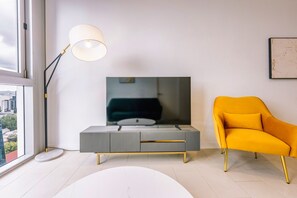 Een moderne woonkamer met een flatscreen televisie op een grijze console, een gele fauteuil en een vloerlamp.