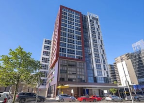A multi-story hotel with a modern facade, a covered entrance, and a parking lot with several cars. - 1 Bedroom Cityside Residence (Fortitude Valley)