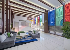Een moderne lobby met een receptiebalie, een zithoek en grote ramen met kleurrijke kunstwerken.