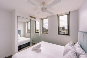 Ein Hotelzimmer mit Bett, Deckenventilator, Fenster mit Stadtblick und Spiegel, der das Bett reflektiert.
