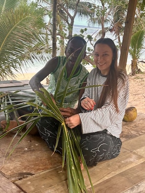 Two people sitting on a wooden deck with palm trees and a beach in the background.