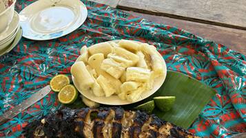 A meal with grilled fish, plantains, and lime on a table with a tropical patterned tablecloth.