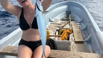 A person on a boat holding a fish, with a clear view of the ocean and a cloudy sky.