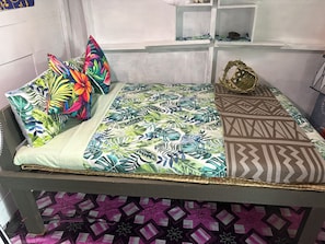 A bed with a tropical leaf pattern bedspread, a geometric patterned pillow, and a woven basket on the side.
