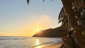 A hammock on a beach with a sunset in the background.