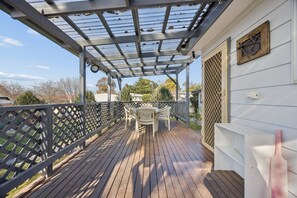 A covered outdoor deck with a table and chairs, a metal railing, and a building with a lattice window.