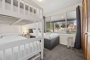 A room with bunk beds, a sofa, a radiator, and a large window with curtains.