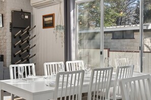 A dining area with a white table and chairs, a wine rack, and a window with a view of trees.