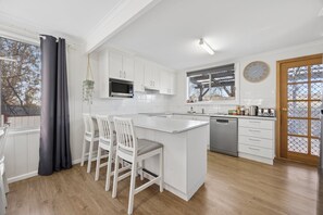 A modern kitchen with white cabinetry, a central island, and a dining area with white chairs.