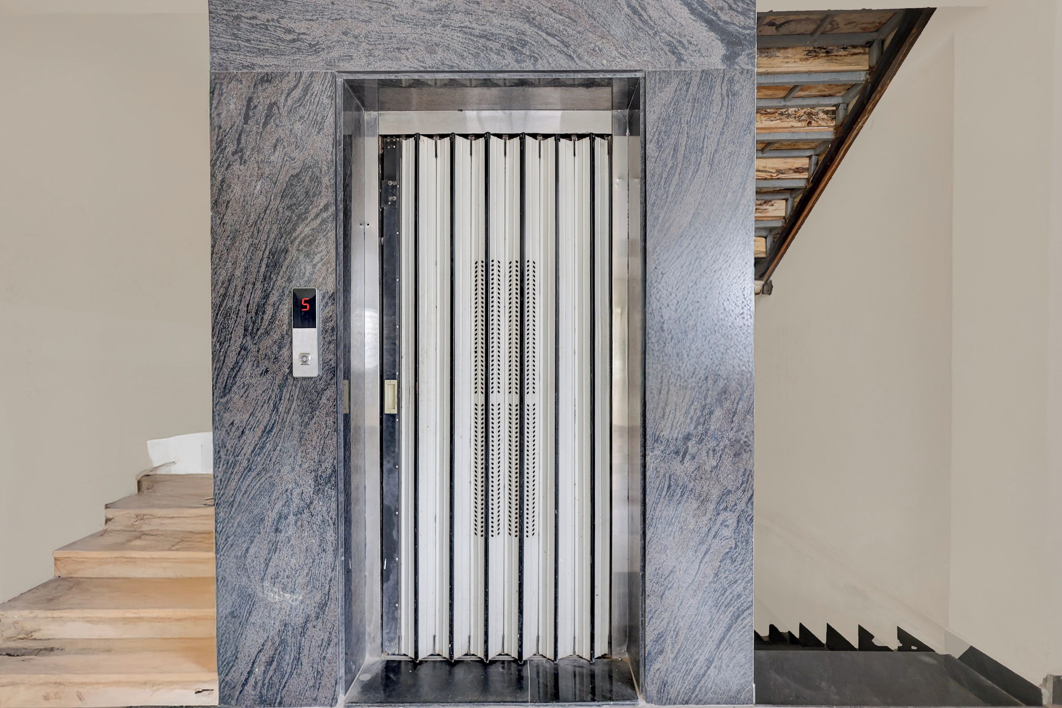 An elevator with a digital display, metallic interior, and a marble wall.