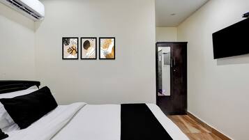 A hotel room with a bed, a flat-screen TV mounted on the wall, and three framed artworks above the bed.