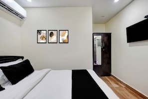 Habitación de hotel con cama, televisor de pantalla plana montado en la pared y tres cuadros enmarcados sobre la cama.