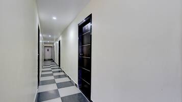 Un couloir avec un sol à carreaux, des murs blancs et une porte noire portant un numéro.